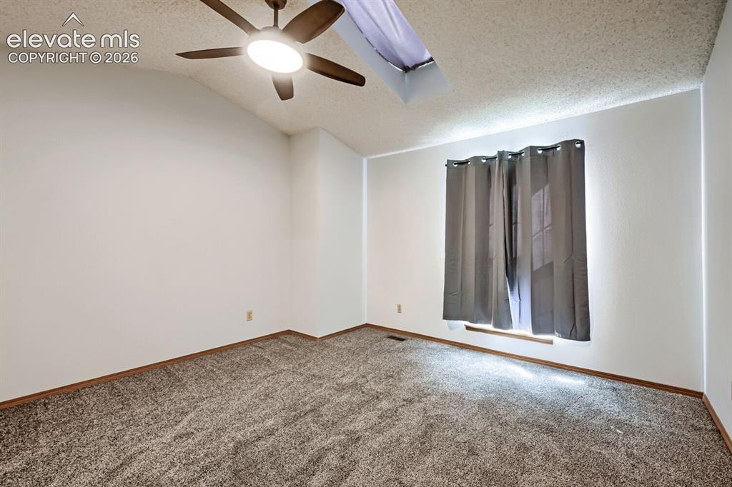 Image 12 of 23: Vaulted ceiling with a ceiling fan, textured ceiling, window with curtain r