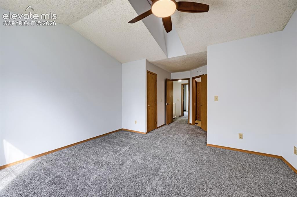 Image 13 of 23: Vaulted ceiling with a ceiling fan, grey carpeting, wood trim, and multiple