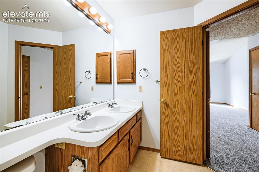 Image 15 of 23: Dual-sink vanity with wood-finish cabinetry, white countertop, and chrome f