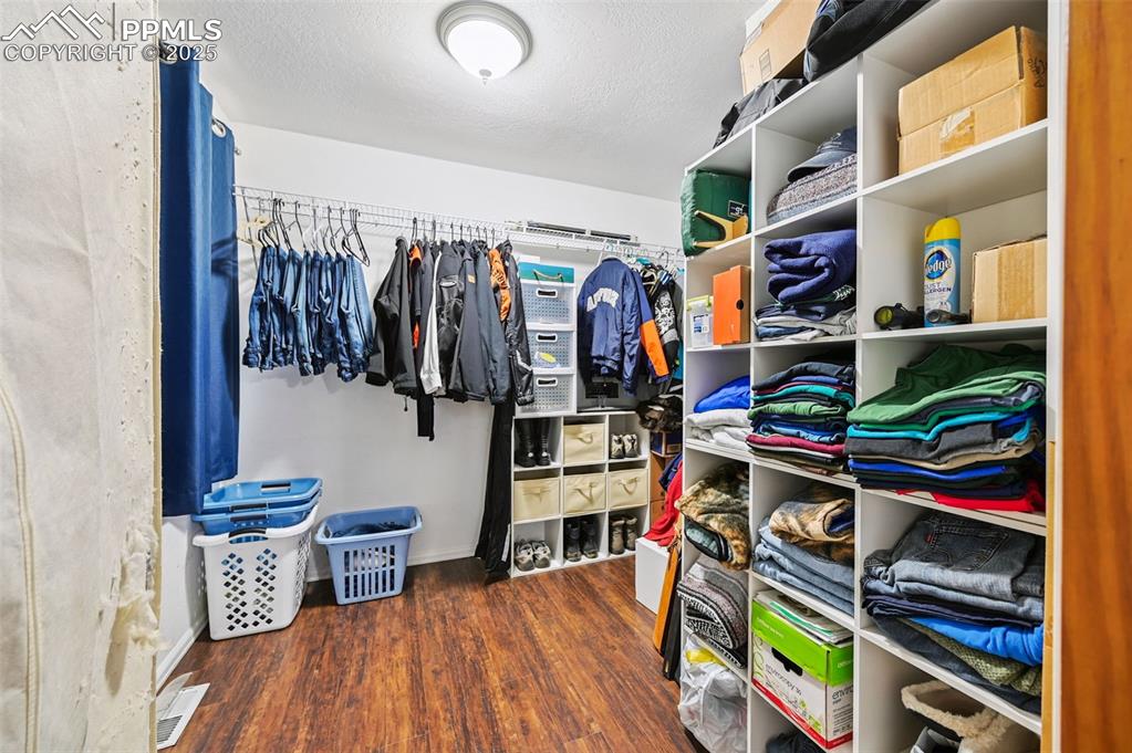 Image 21 of 43: Walk in closet with dark wood-style floors