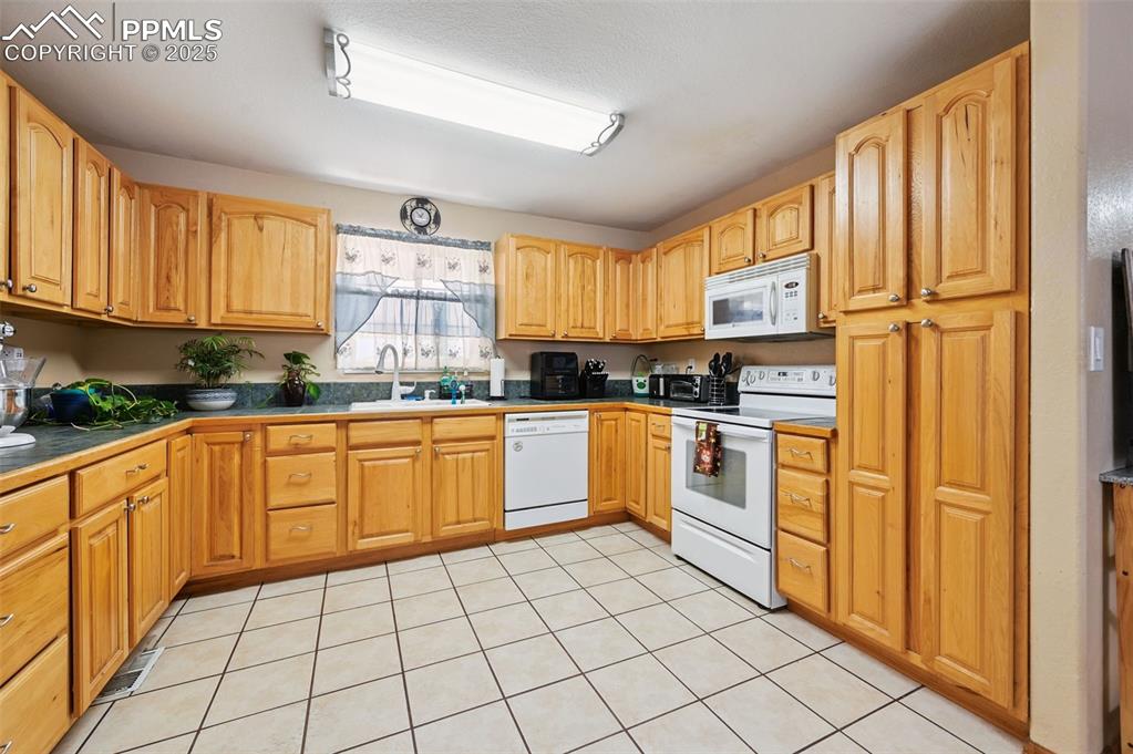 Image 7 of 43: Kitchen with dark countertops, white appliances, and light tile patterned f
