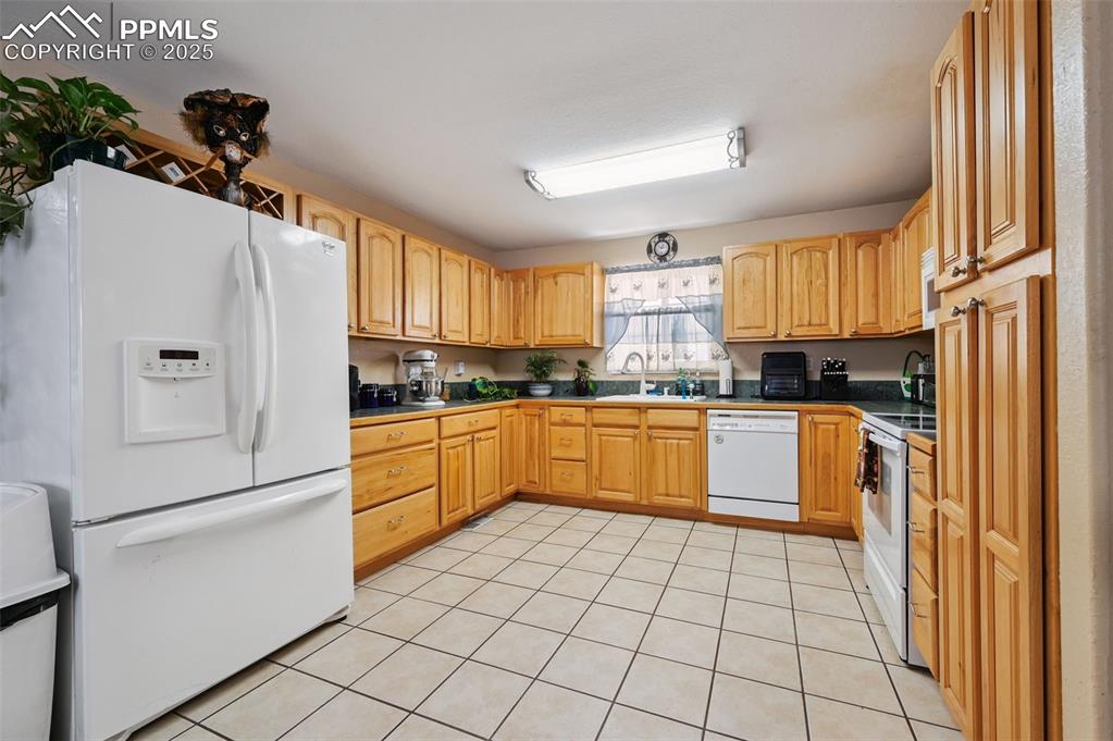 Image 8 of 43: Kitchen featuring dark countertops, white appliances, light tile patterned 