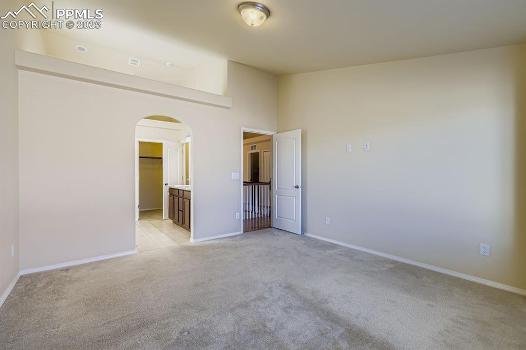 Image 11 of 31: Primary bedroom with arched walkways, light carpet, and ensuite bath
