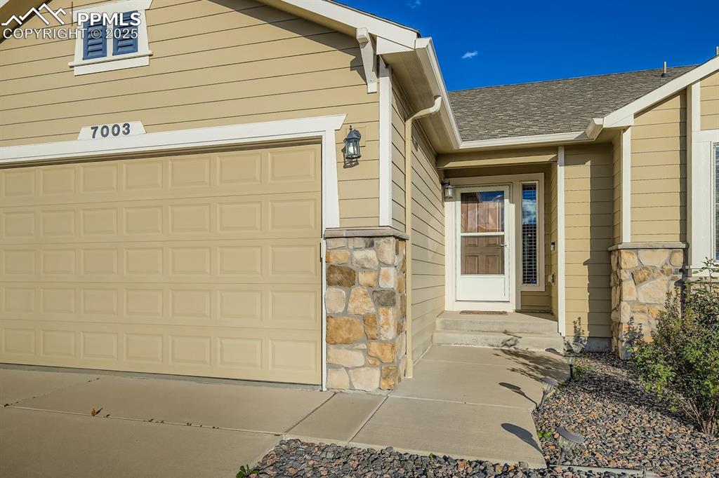 Image 3 of 31: Doorway to property with stone siding, roof with shingles, and driveway
