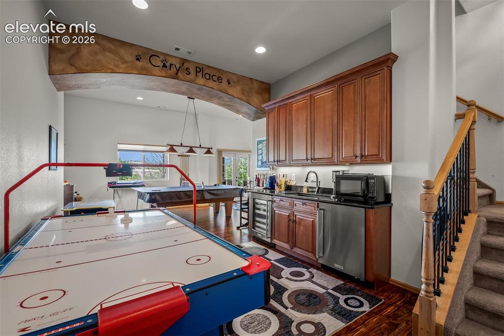Image 34 of 50: Entertainment room featuring a wet bar with wood cabinetry, dark countertop