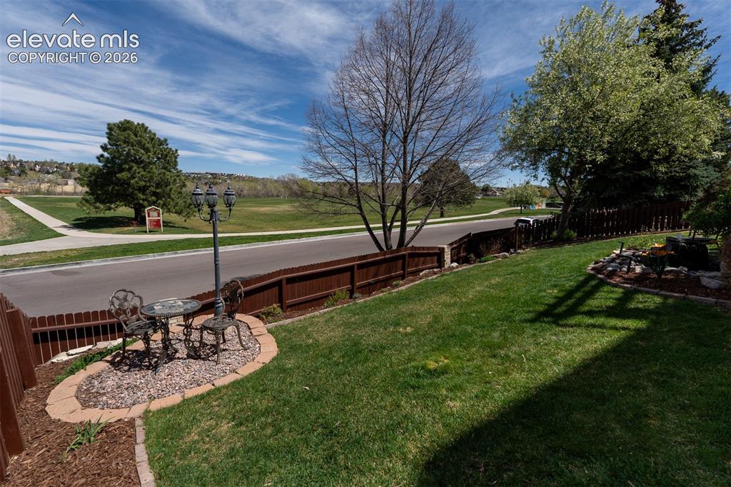 Image 45 of 50: Lush green, back yard lawn with a decorative garden bed featuring a street