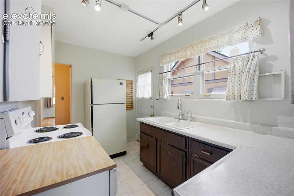 Image 10 of 46: Kitchen featuring white appliances, track lighting, and a double basin sink
