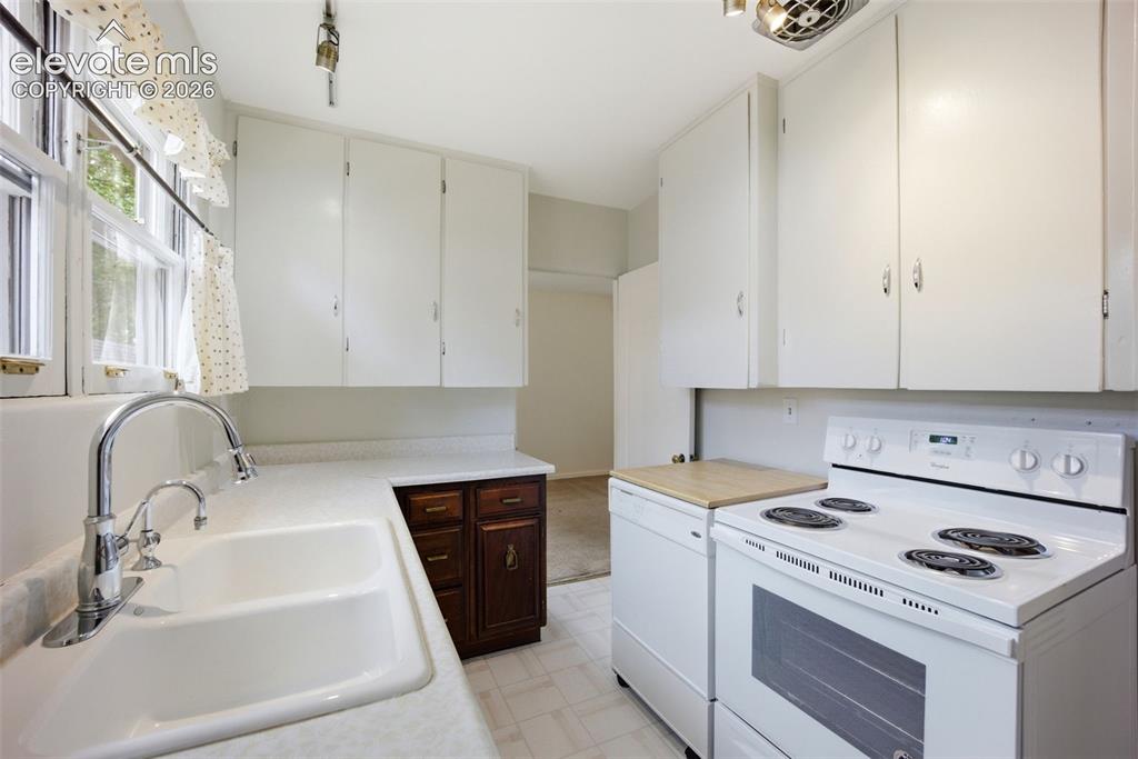 Image 12 of 46: Kitchen featuring white upper cabinetry, a double basin sink with chrome fa