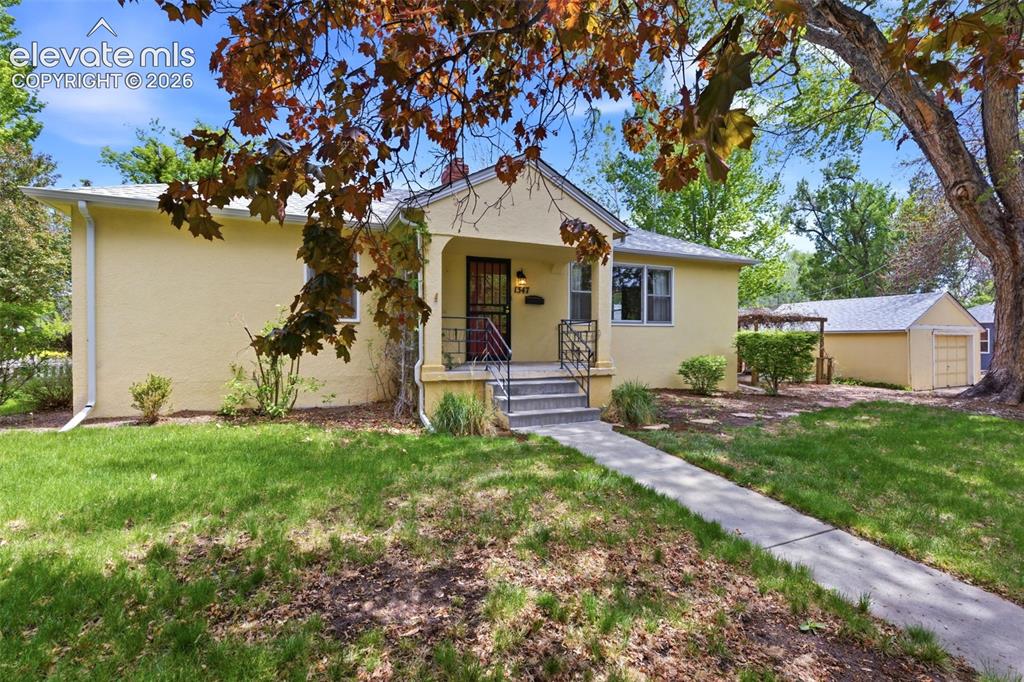 Image 2 of 46: Yellow stucco exterior featuring a covered front porch with iron railings, 