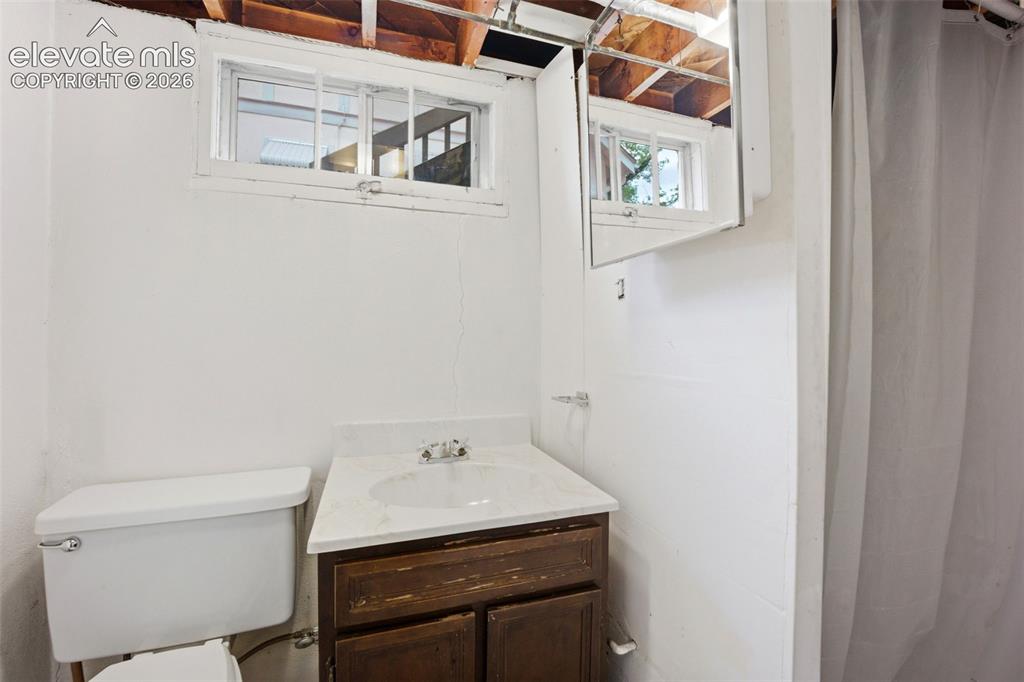Image 28 of 46: Compact bathroom featuring a window, white walls, and an exposed wood ceili