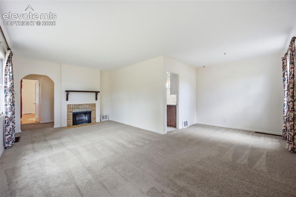 Image 5 of 46: Spacious living area featuring a brick fireplace with a dark wood mantel, l