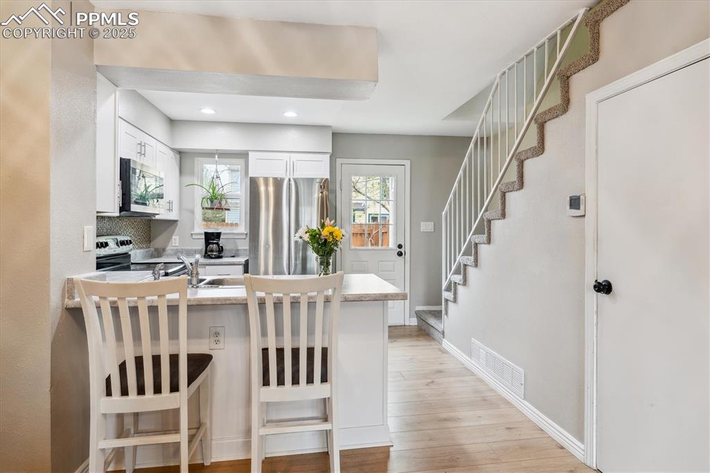 Image 10 of 24: Kitchen with visible vents, a peninsula, light wood-style floors, white cab