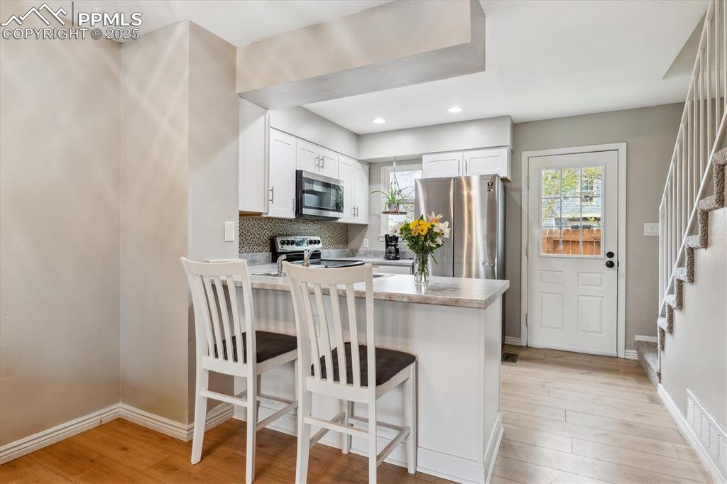 Image 9 of 24: Kitchen with a kitchen breakfast bar, light countertops, white cabinets, a