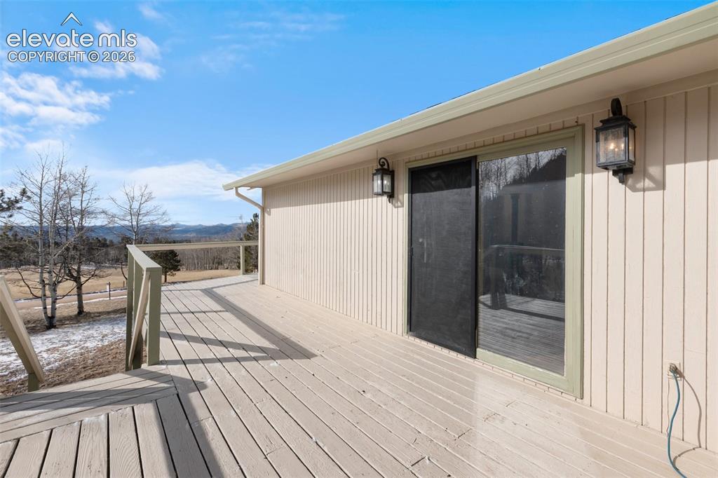 Image 10 of 40: Expansive wood-finish deck with railing, exterior wall lanterns, and slidin