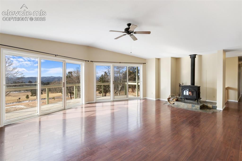 Image 12 of 40: Vaulted ceiling with a ceiling fan, wood-finish flooring, wood-burning stov