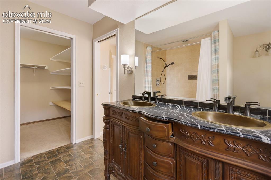 Image 23 of 40: Dual vanity with dark stone countertop, ornate wood cabinetry, and vessel s