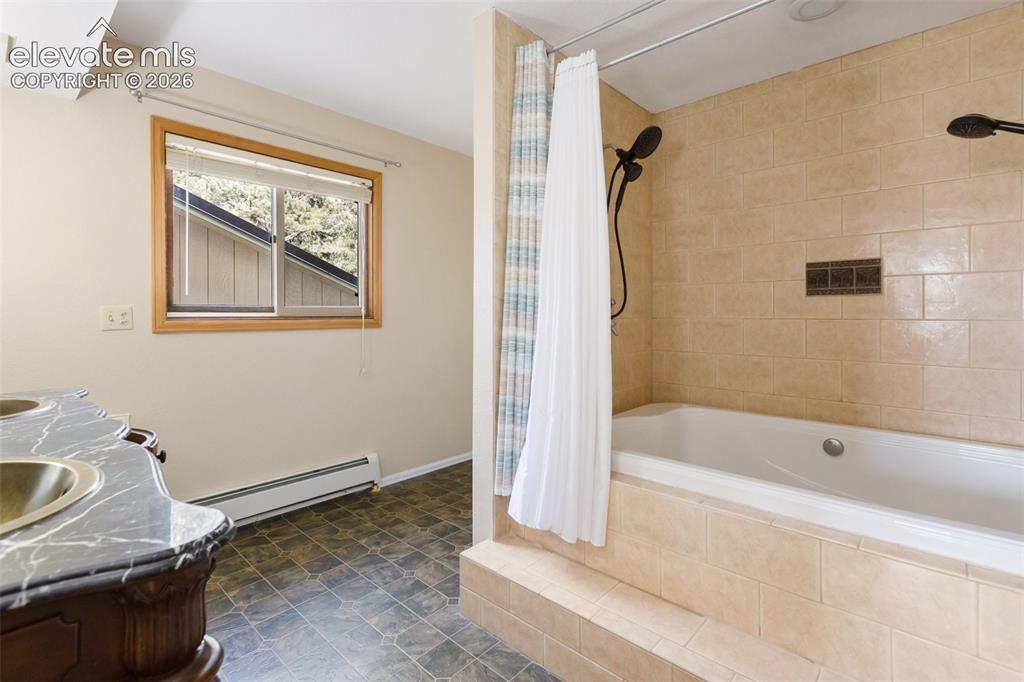 Image 24 of 40: Tile-surround soaking tub with dual shower heads, wood-framed window, and a