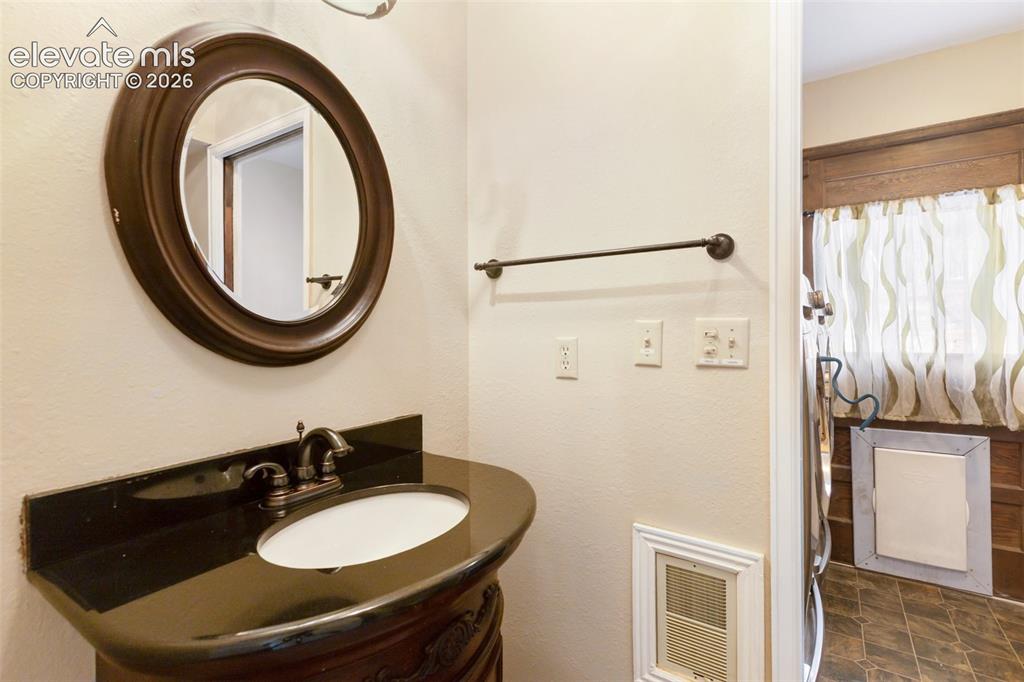Image 26 of 40: Vanity with a dark countertop, an oval undermount sink, and a bronze-finish