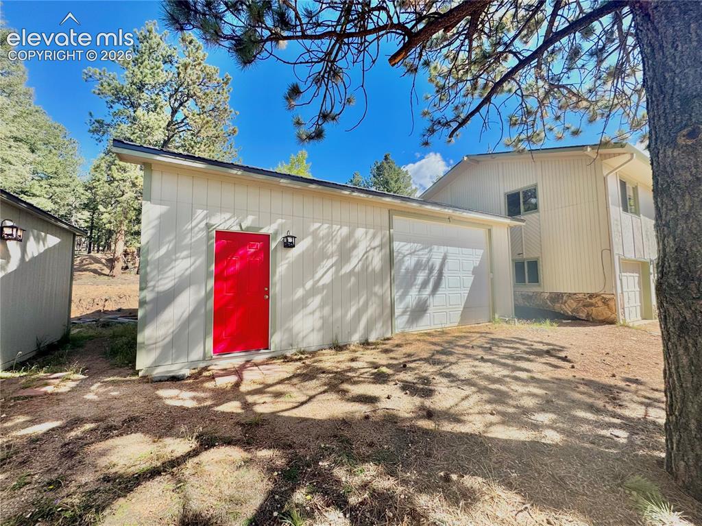 Image 7 of 40: Detached Garage/Shop with red entry door, exterior lighting, and a single-c