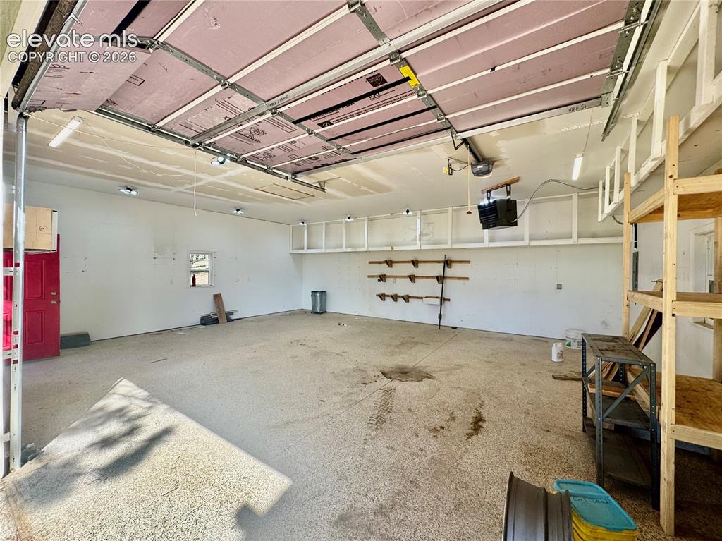 Image 9 of 40: Spacious garage with exposed insulation on the overhead door, multiple fluo