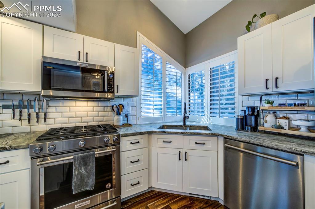 Image 15 of 29: Kitchen with stainless steel appliances, white cabinetry, and dark stone co