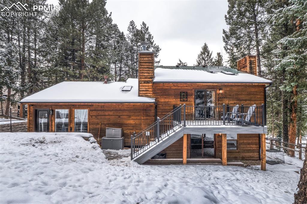 Image 3 of 29: Snow covered property with a chimney, stairs, a deck, and a metal roof