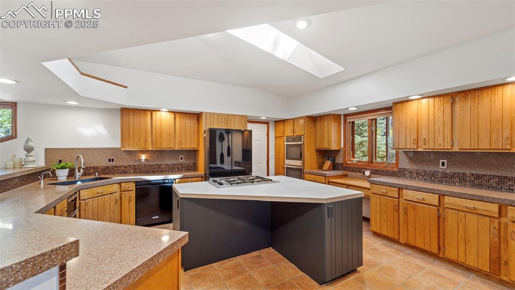 Image 12 of 46: Kitchen with tasteful backsplash, a skylight, black appliances, brown cabin