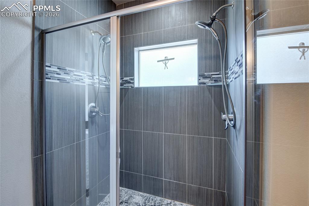 Image 18 of 36: The shower features gray subway tile, a decorative mosaic tile band, a glas