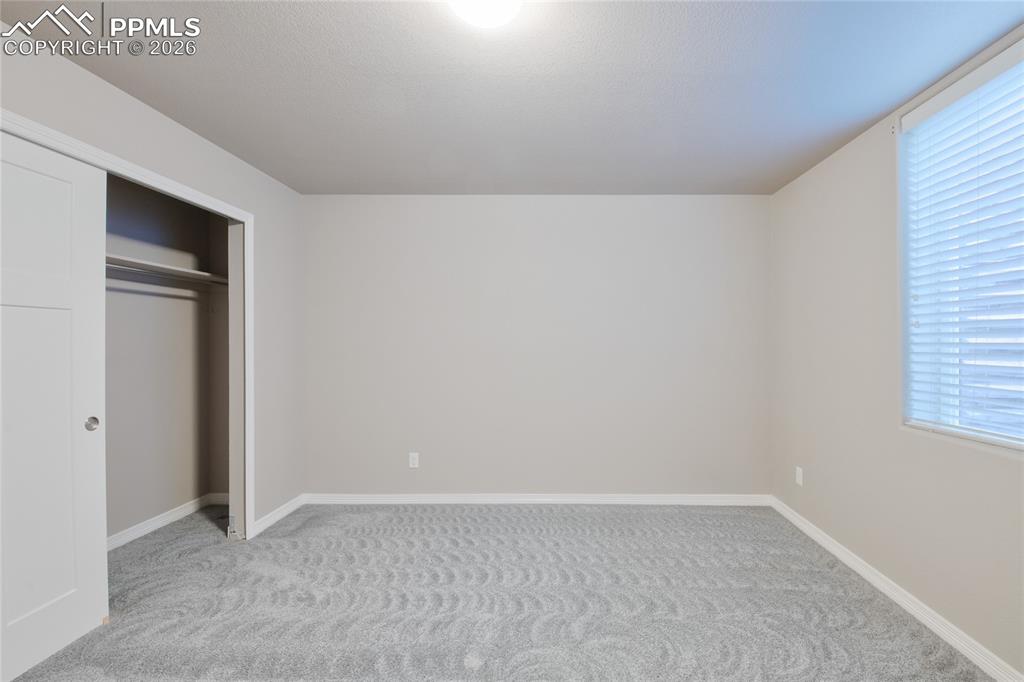 Image 28 of 36: This room features light grey walls, grey patterned carpeting, and a window