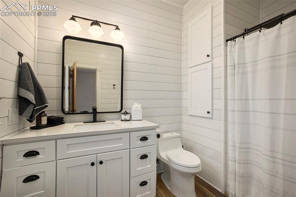 Image 14 of 38: Bathroom with wood walls, a shower with shower curtain, vanity, and dark wo