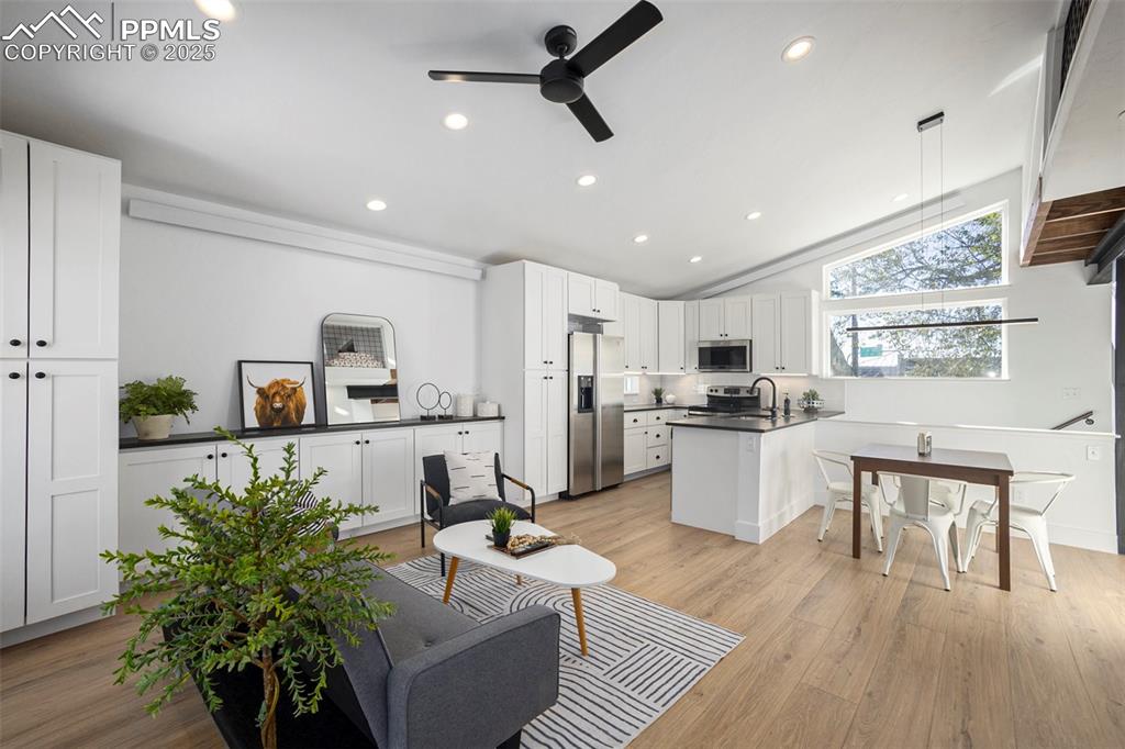 Image 21 of 38: Living area with vaulted ceiling, light wood finished floors, ceiling fan,