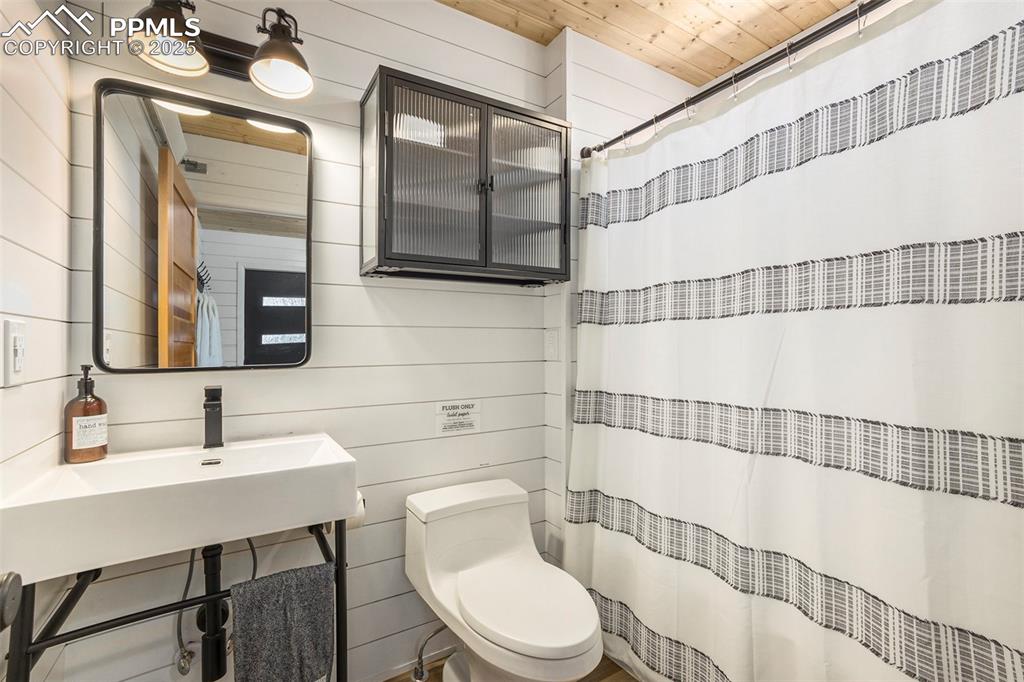 Image 30 of 38: Bathroom with a shower with curtain and wood walls