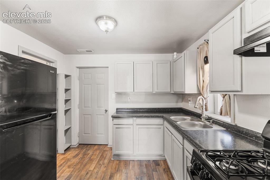 Image 10 of 23: Kitchen featuring wood-finish flooring, white cabinetry, dark countertops,
