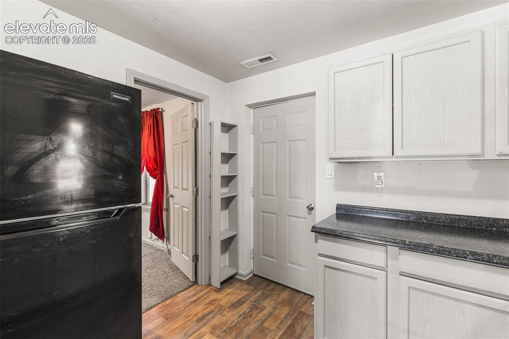 Image 12 of 23: Wood-finish flooring, white cabinetry with dark countertops, built-in shelv