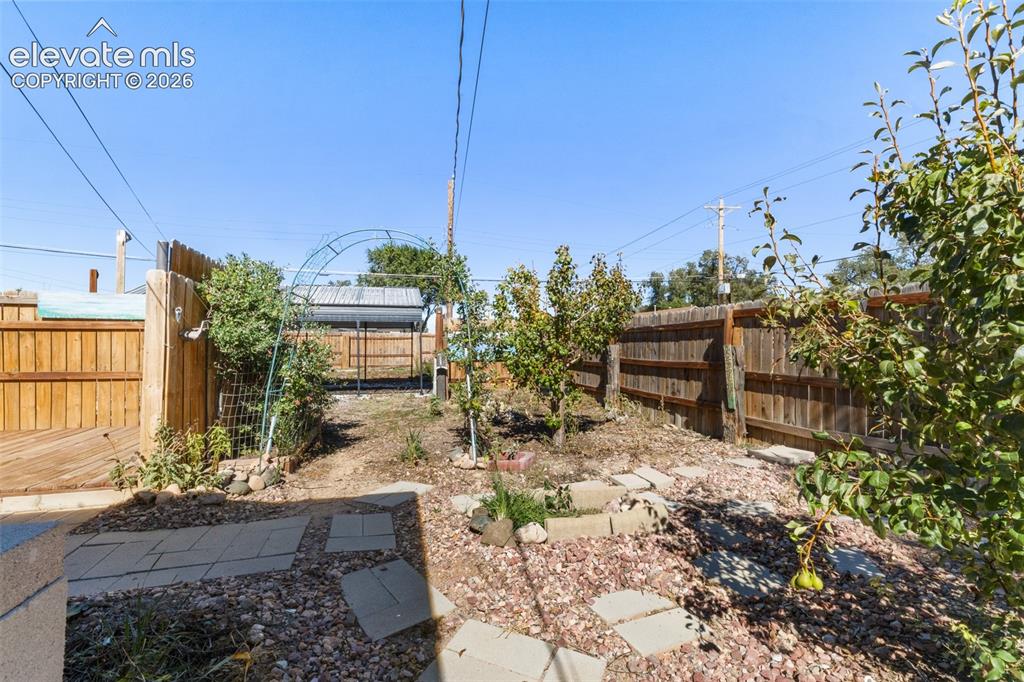 Image 19 of 23: Backyard space featuring a wooden fence, stone paver pathway, mature trees,