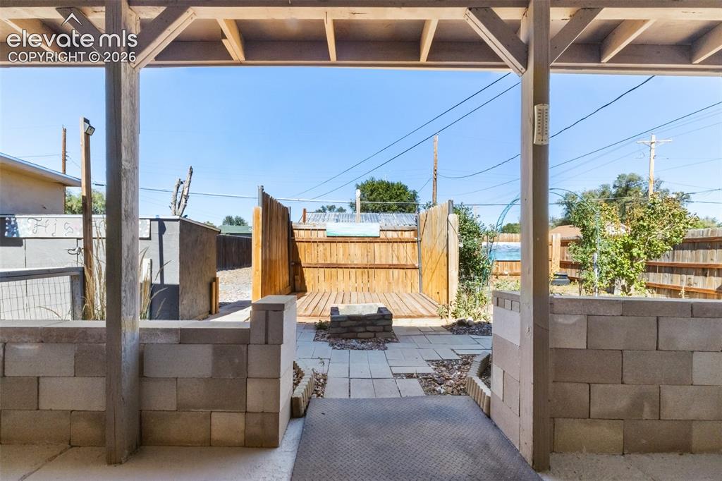 Image 20 of 23: Covered patio with exposed wood beams, concrete block half-walls, and a met