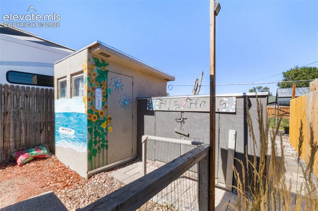Image 23 of 23: Storage shed with decorative exterior, dual windows, and fenced perimeter