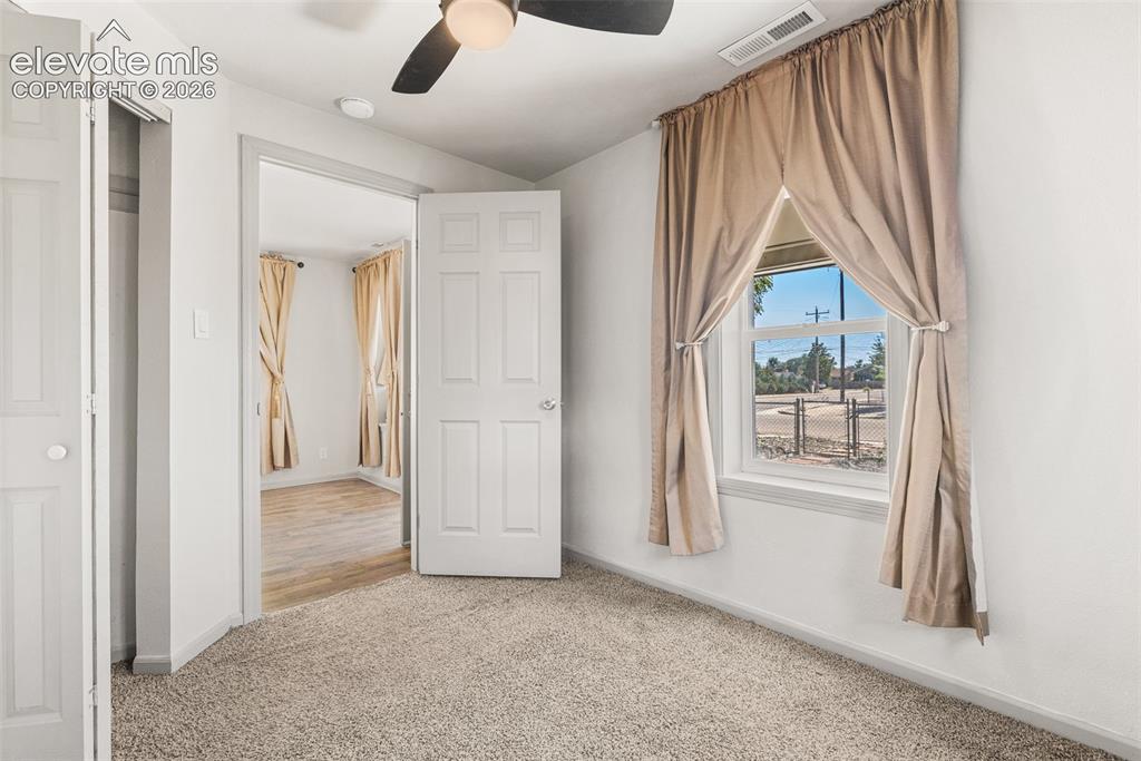 Image 8 of 23: Carpeted flooring, white six-panel door, ceiling fan, and window with natur