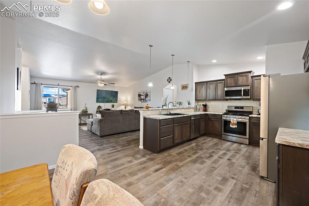 Image 17 of 36: Kitchen featuring open floor plan, dark brown cabinets, vaulted ceiling, ap