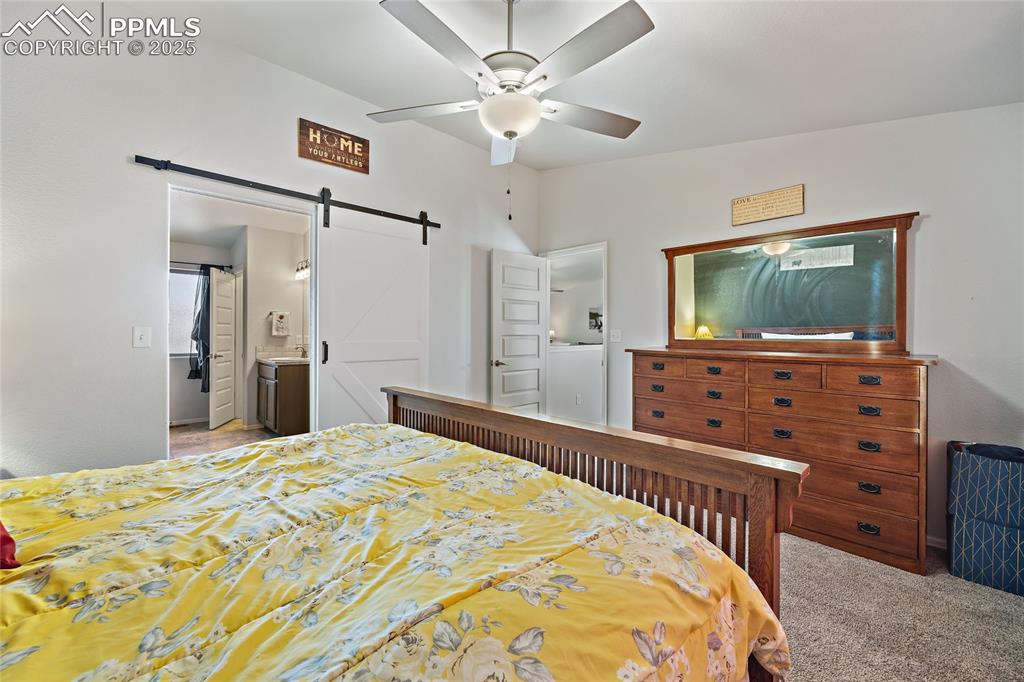 Image 29 of 36: Bedroom featuring a barn door, ensuite bathroom, light colored carpet, and