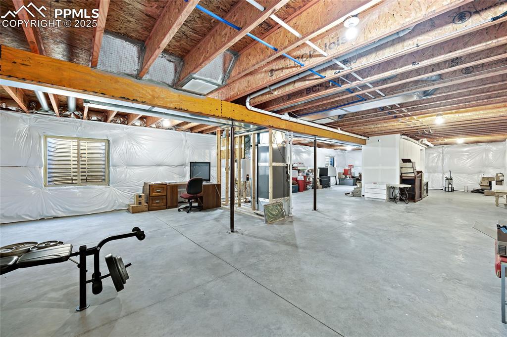 Image 33 of 36: Unfinished below grade area with a desk and heating unit