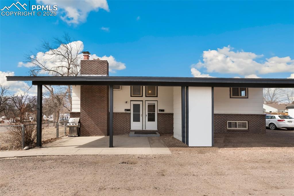 Caption: View of front of home with brick siding, a chimney, and fence