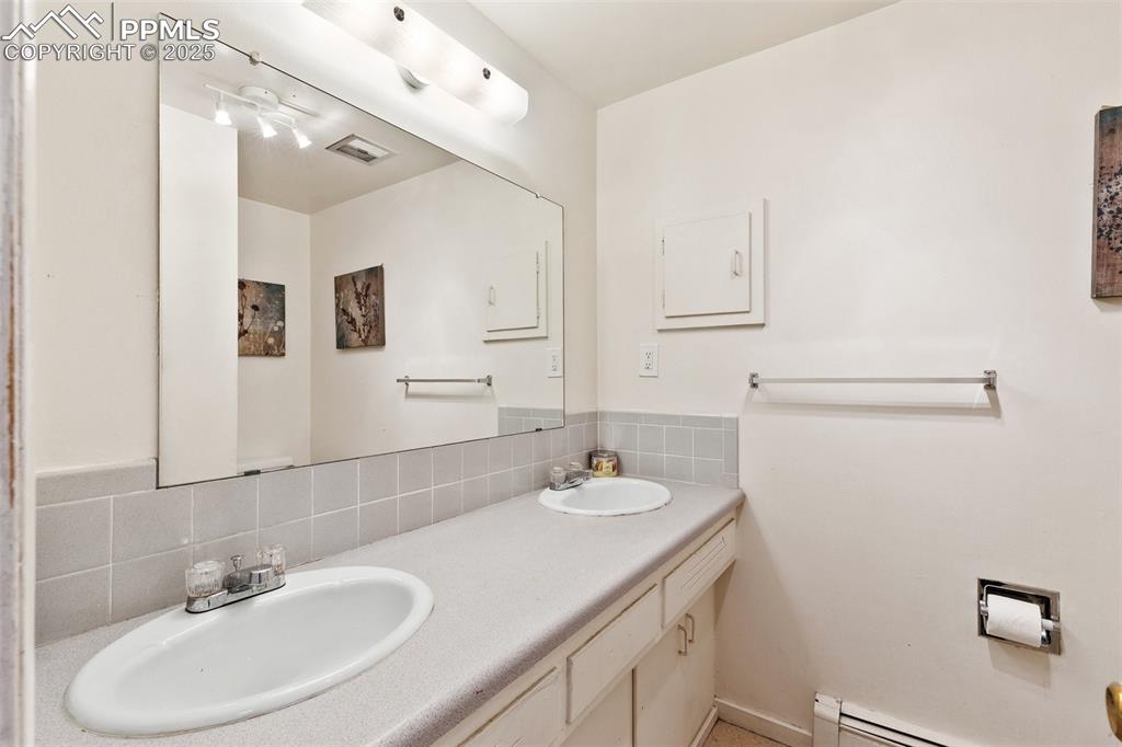 Image 23 of 49: Bathroom with double vanity, backsplash, a baseboard radiator, and a sink