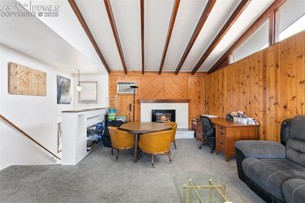 Image 24 of 49: Living area with wooden walls, lofted ceiling with beams, a wall unit AC, c