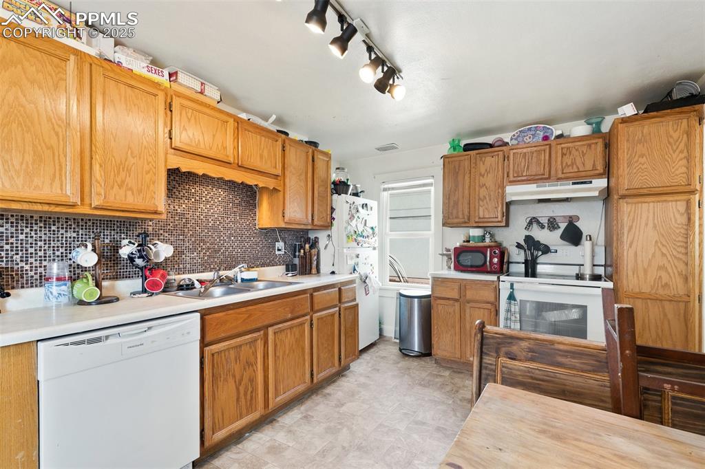 Image 41 of 49: Kitchen with under cabinet range hood, a sink, tasteful backsplash, white a