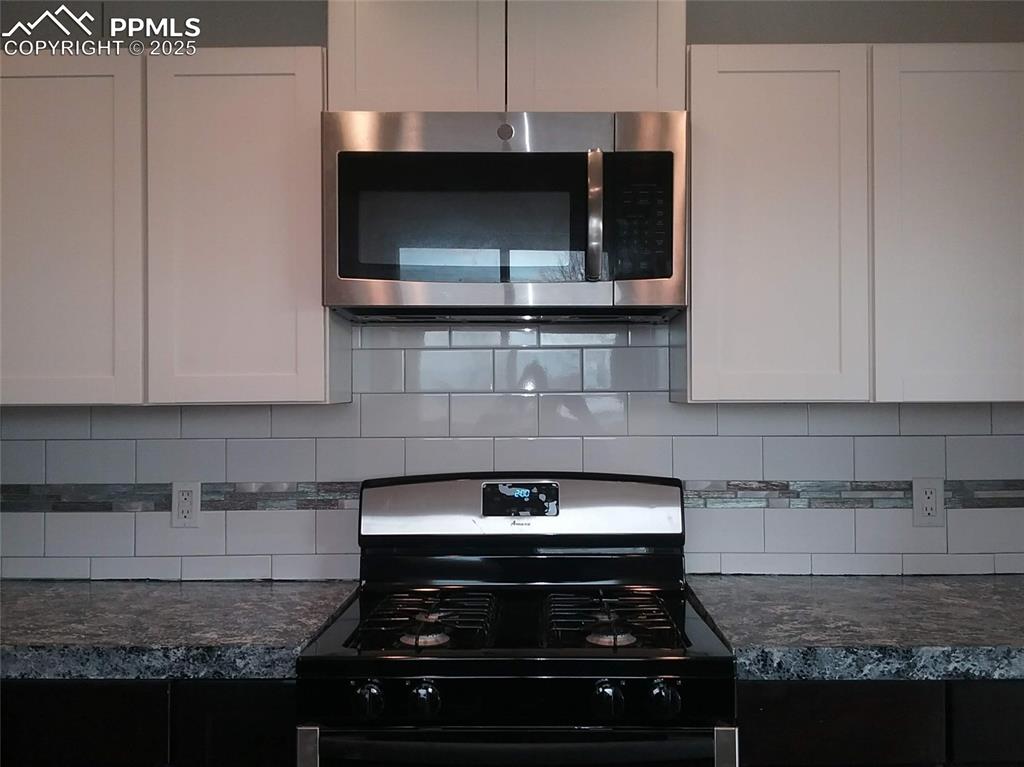 Image 42 of 47: Kitchen with decorative backsplash, stainless steel microwave, white cabine