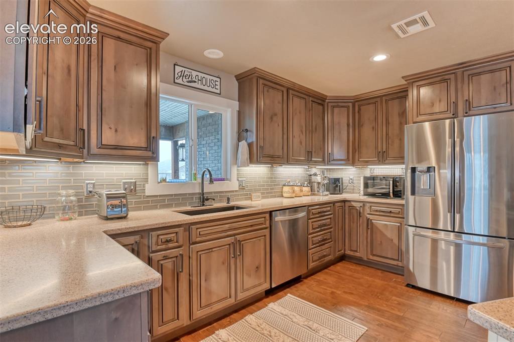 Image 10 of 50: Kitchen with stainless steel appliances, light stone countertops, light woo