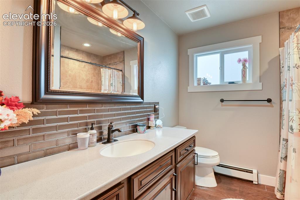 Image 18 of 50: Bathroom with backsplash, vanity, a baseboard radiator, light wood-style fl