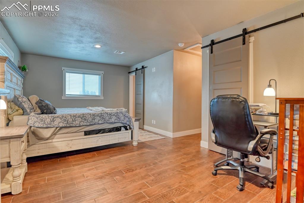 Image 23 of 50: Bedroom with a barn door, light wood-style floors, and a textured ceiling