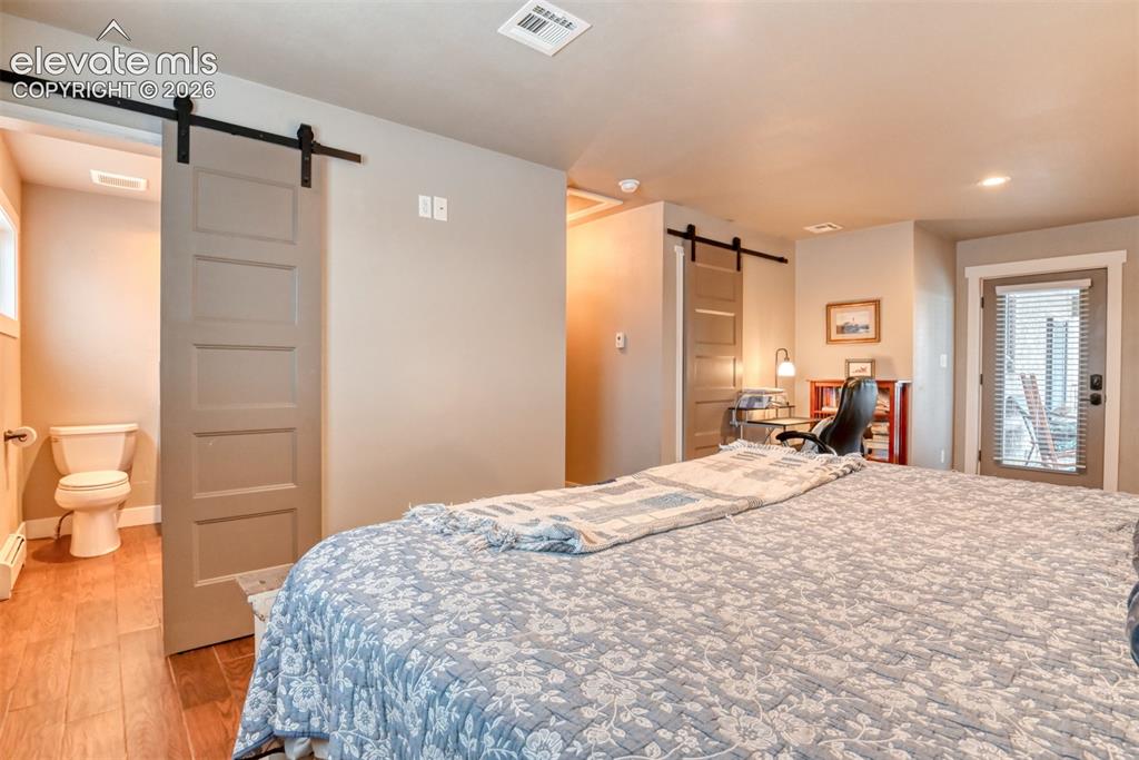 Image 27 of 50: Bedroom featuring a barn door, multiple windows, light wood-style floors, a